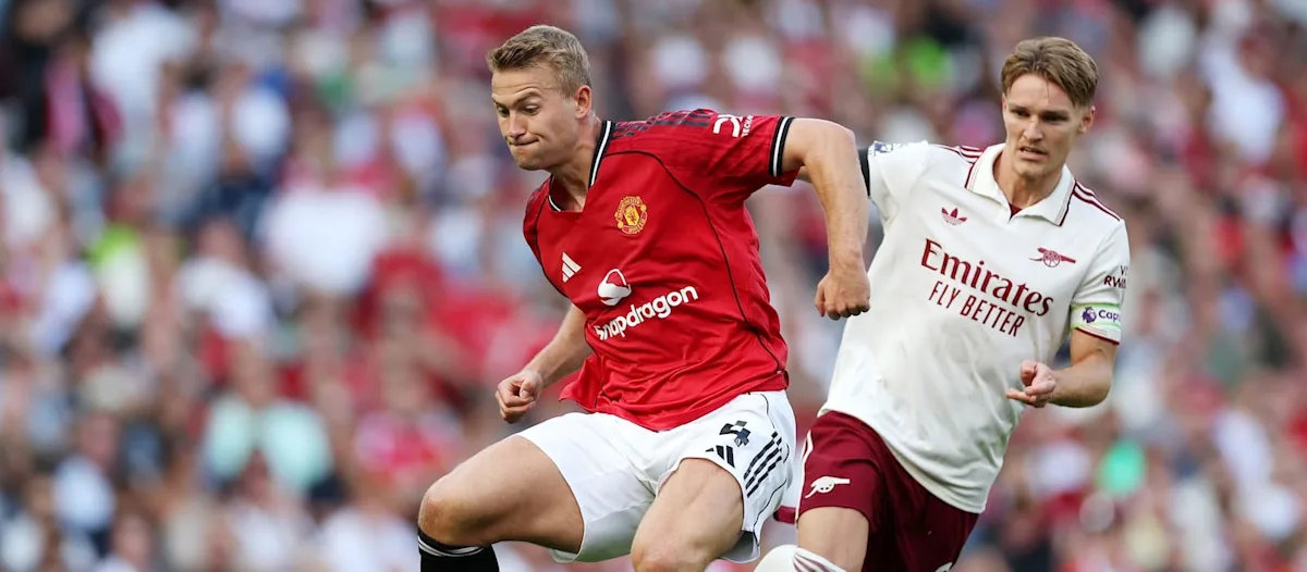 Footballers in red and white kits sprint during a match as a blurred crowd watches