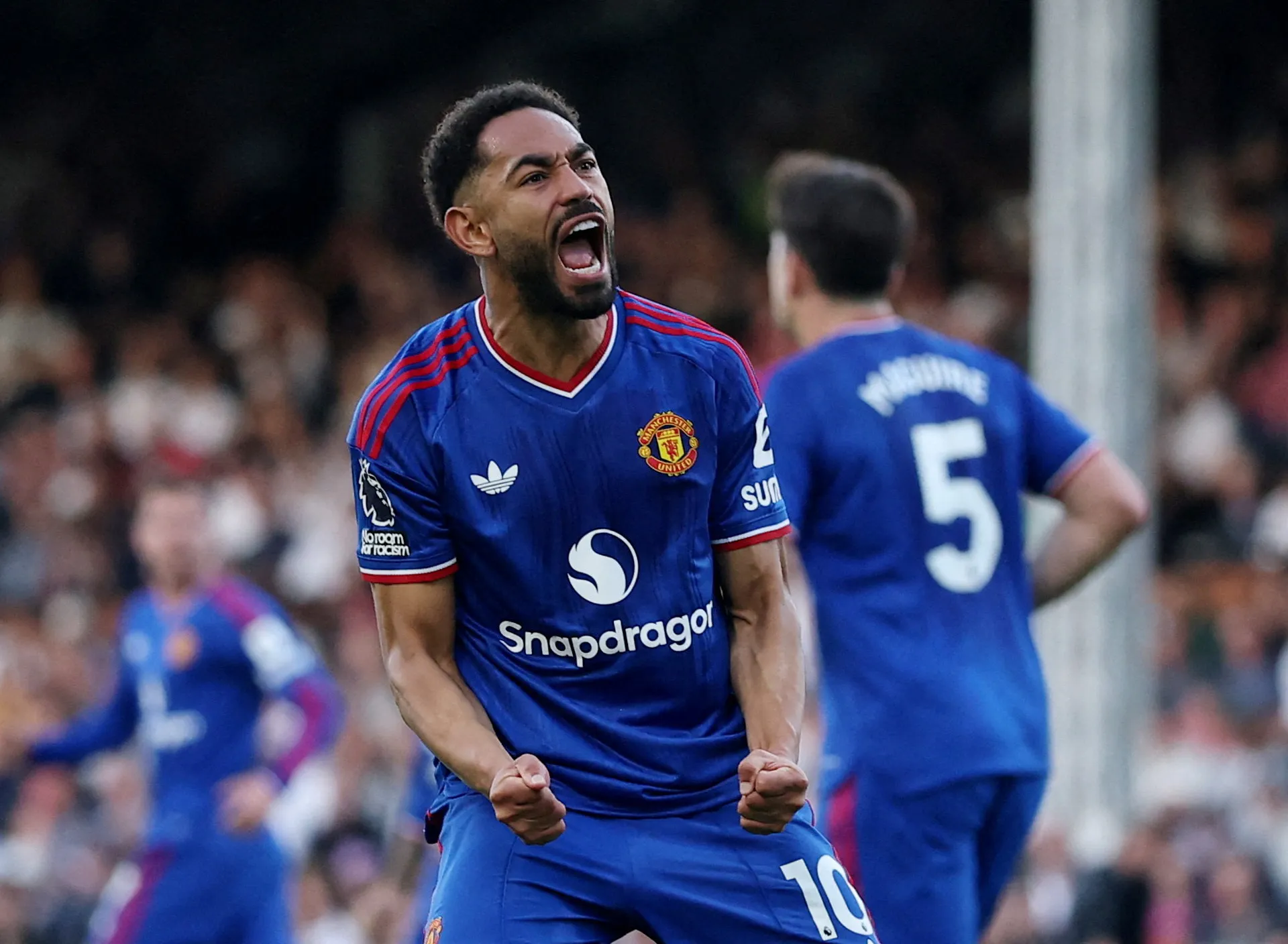 Manchester United player celebrates with clenched fists during a football match as teammates and fans blur behind him