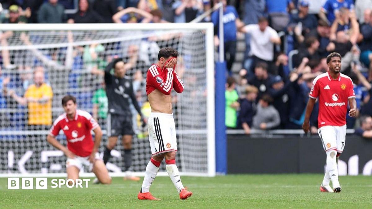 Three Manchester United players react during a match as supporters watch from the stands.