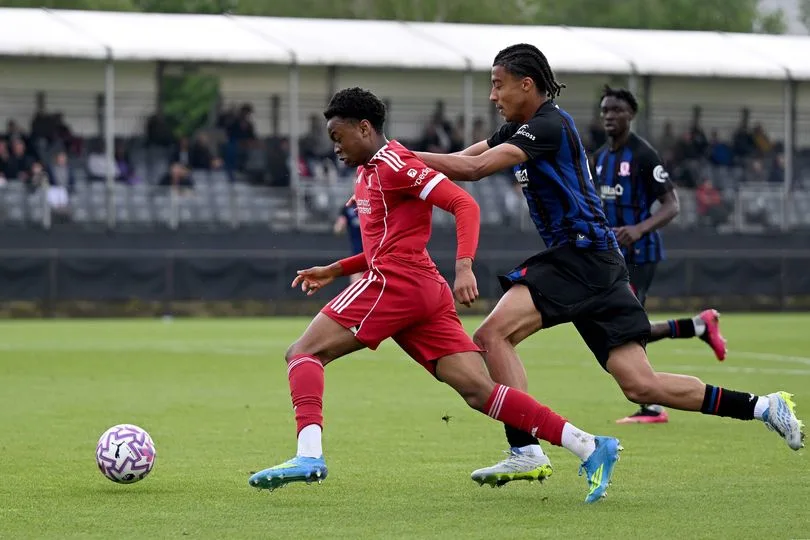 Two young soccer players in red and black kits race for the ball during a match.