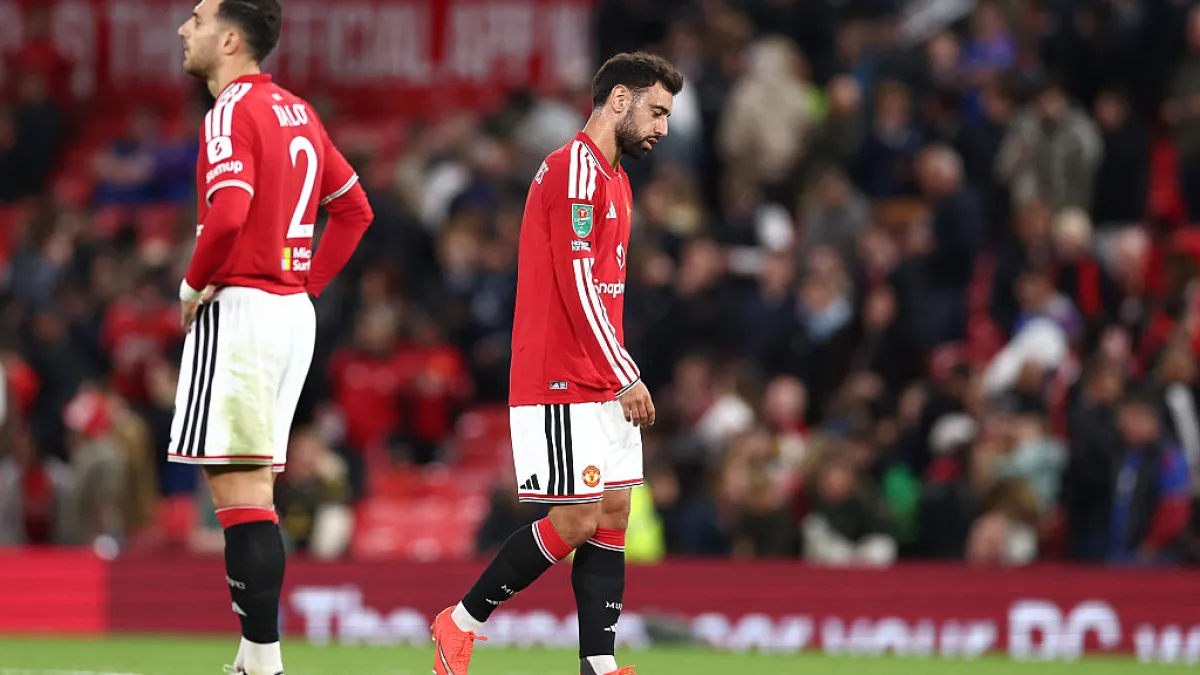 Two Manchester United players in red kits walk across the pitch after a match