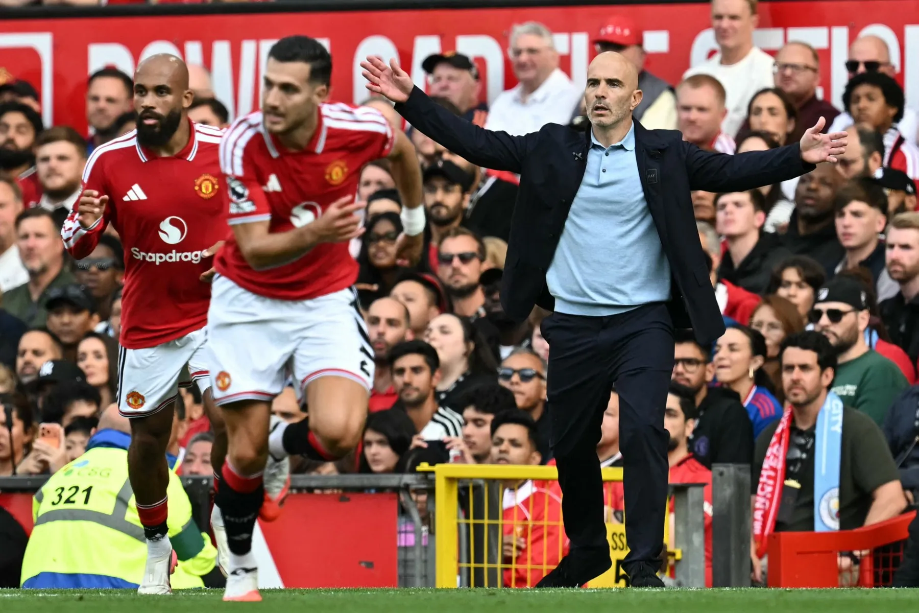 Manchester United players run past a coach gesturing on the touchline during a match.