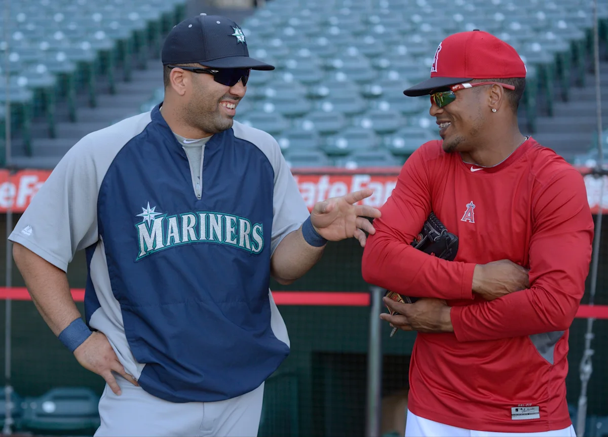 Two baseball players in Mariners and Angels apparel chat near the field wearing sunglasses.