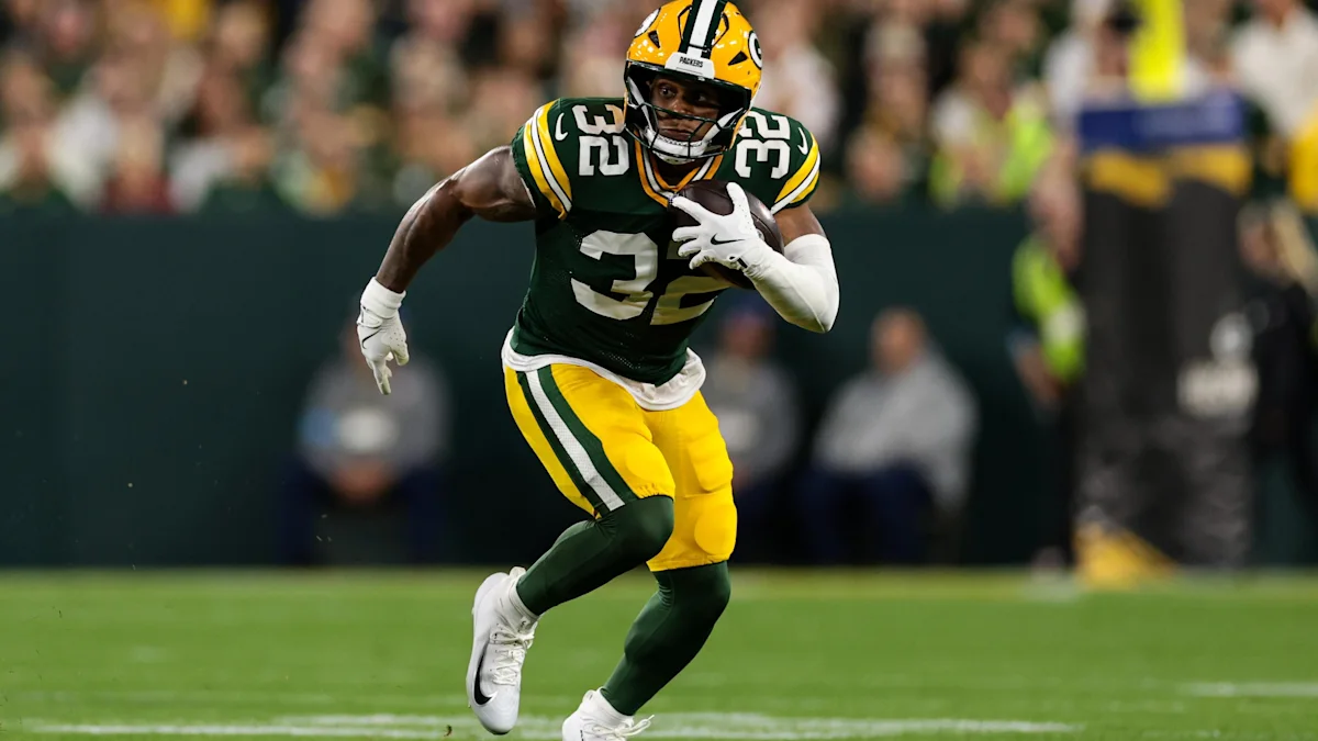A Packers player in a green and yellow uniform runs with the football during a game.