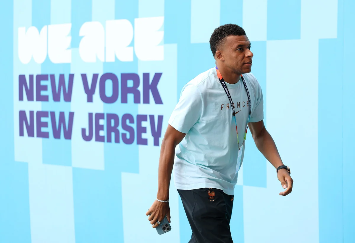 French footballer in a light blue France shirt walks past a New York event backdrop.
