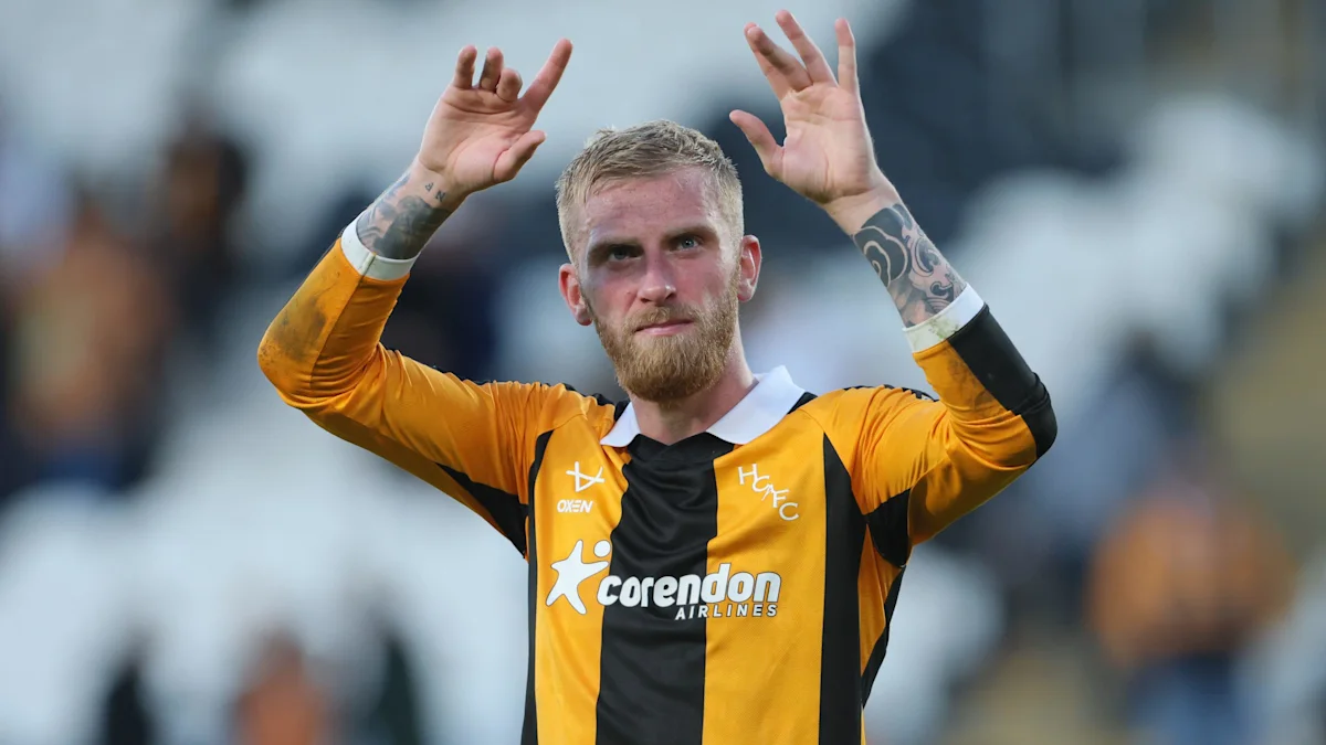 Hull City player in amber and black kit raises both hands toward the crowd