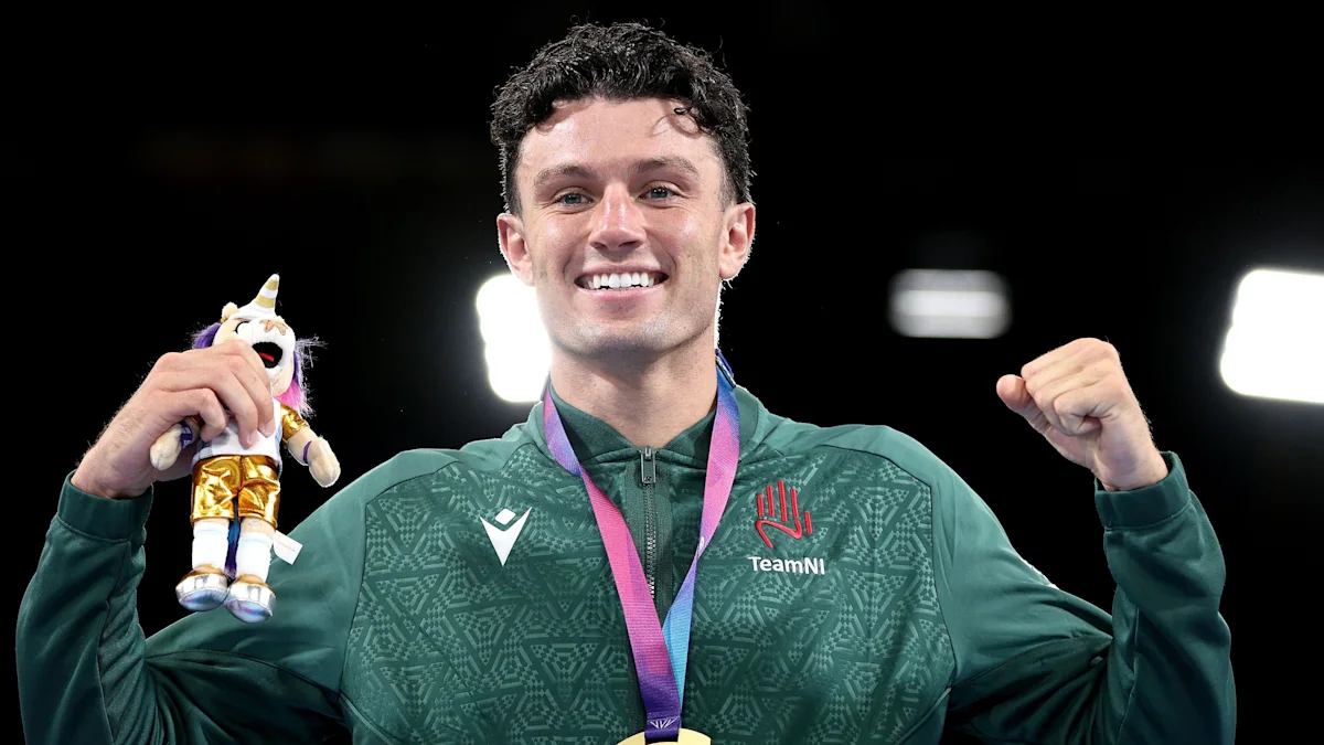 Smiling male athlete raises both fists while holding a unicorn mascot and wearing a medal