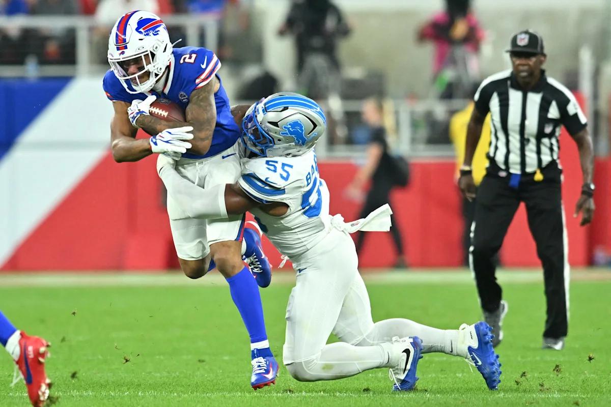 Football player in blue uniform carries the ball while a defender in white makes a tackle