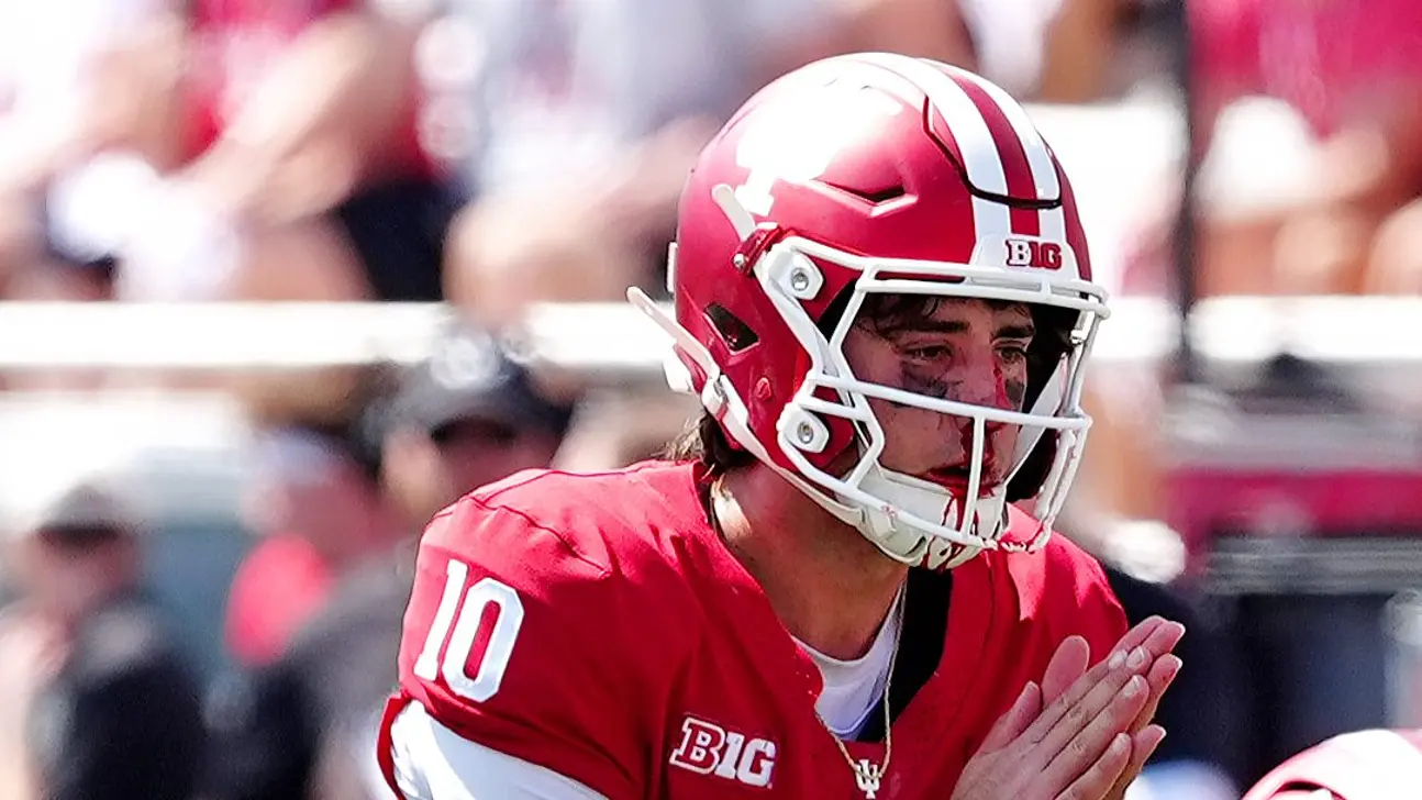 Football quarterback in a red uniform and helmet claps during a game.