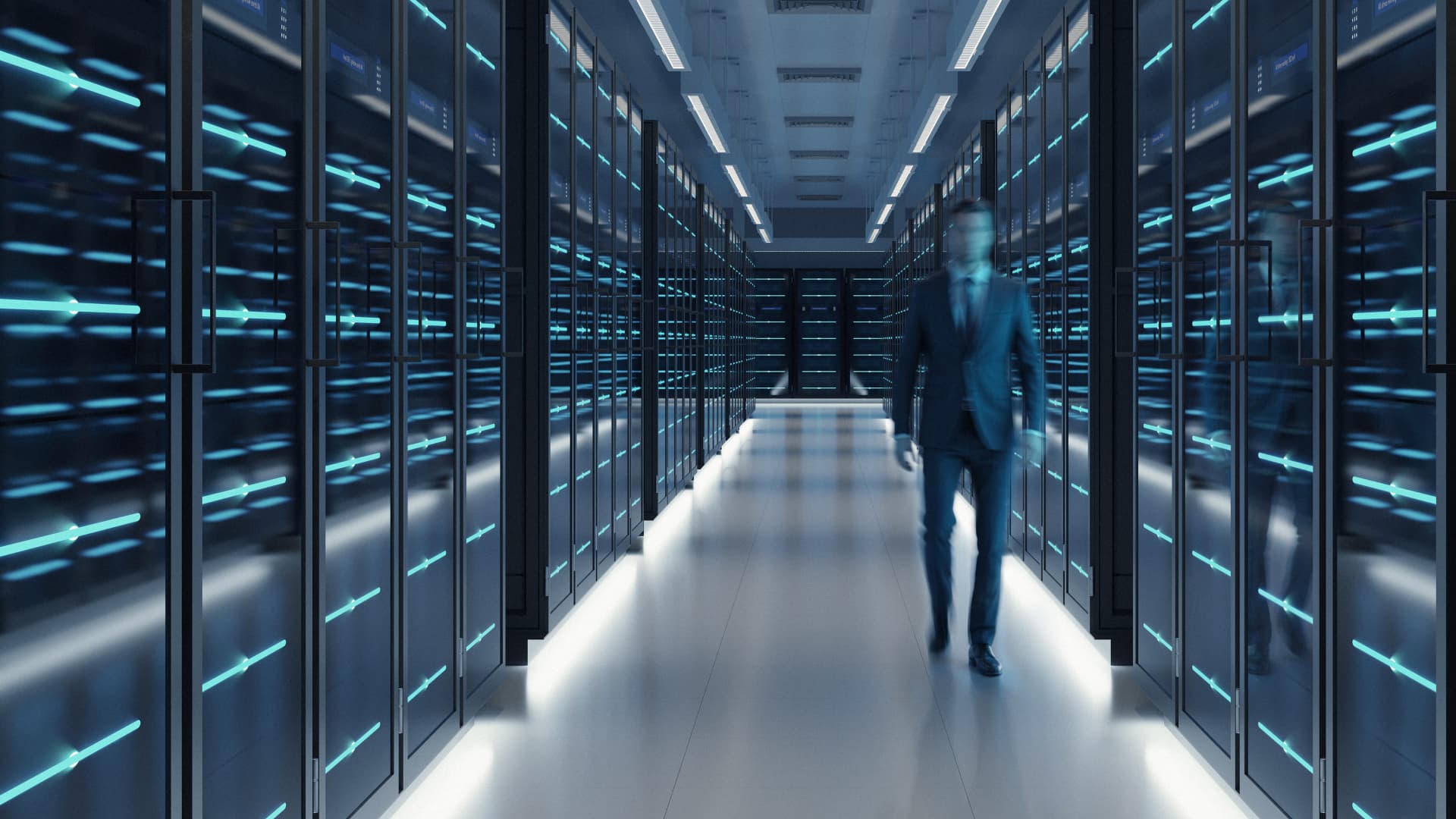 A blurred professional walks through a brightly lit server room lined with glowing blue racks.