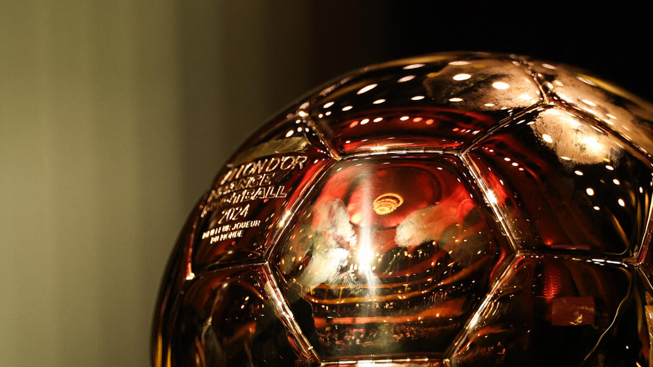 Close-up of the golden Ballon d'Or trophy reflecting bright lights in a dark setting.