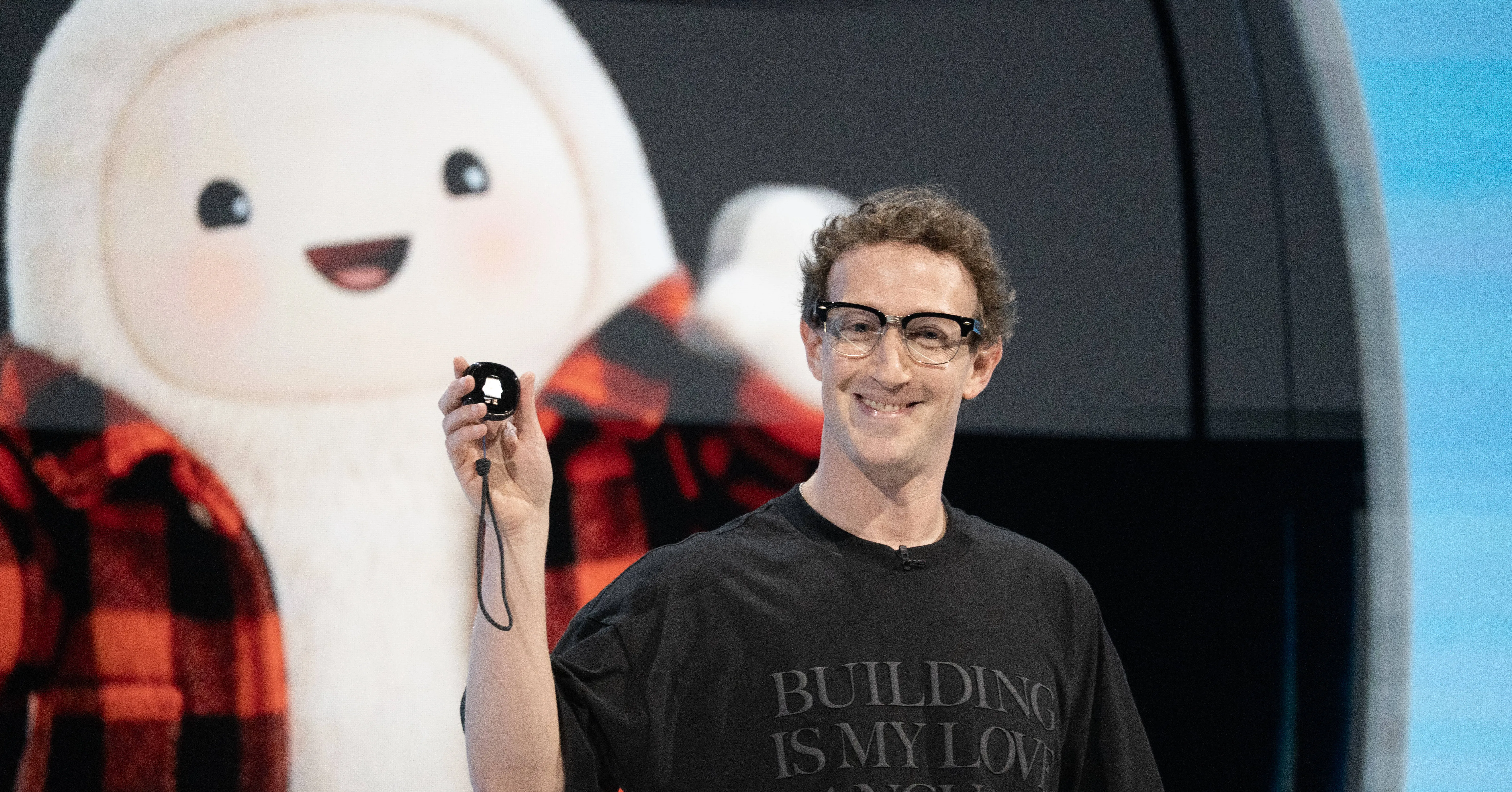A man in glasses holds up a small black device in front of a large cartoon character backdrop.
