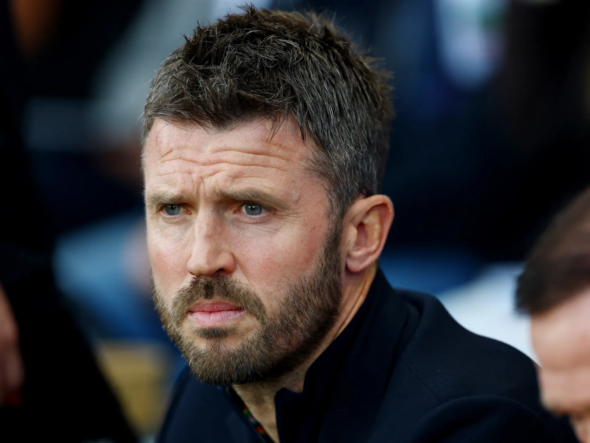 Close-up of a bearded man with short dark hair looking seriously toward the camera