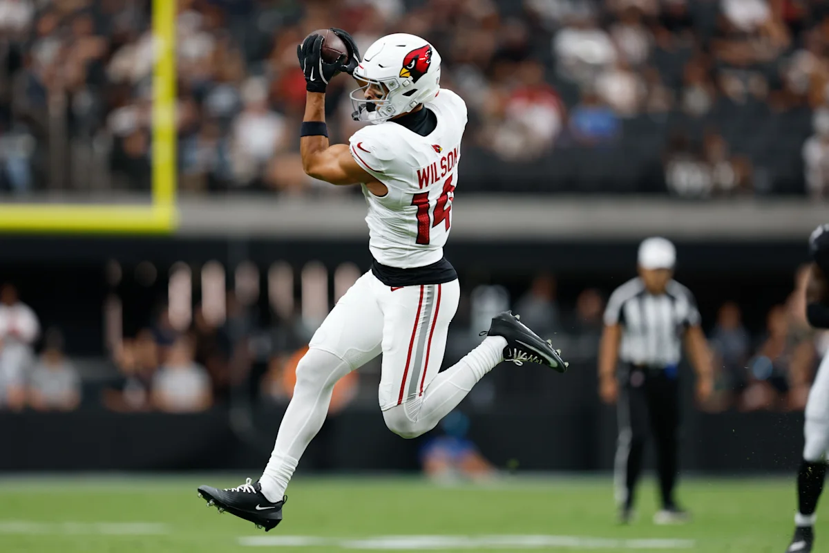 Football player in white Cardinals uniform leaps while catching a pass during a game.