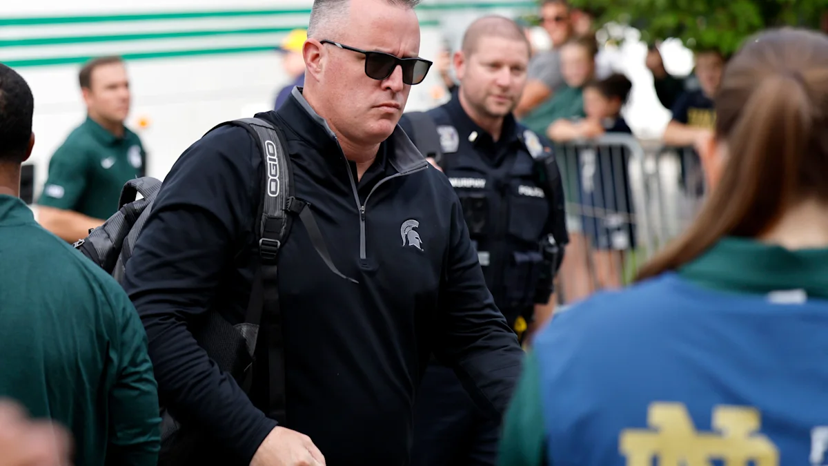A man in sunglasses and a black Michigan State pullover walks past police and spectators.