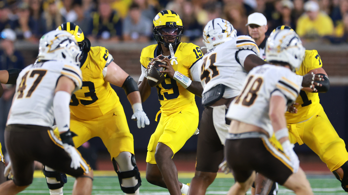Michigan quarterback in a yellow uniform prepares to pass as Western Michigan defenders close in.