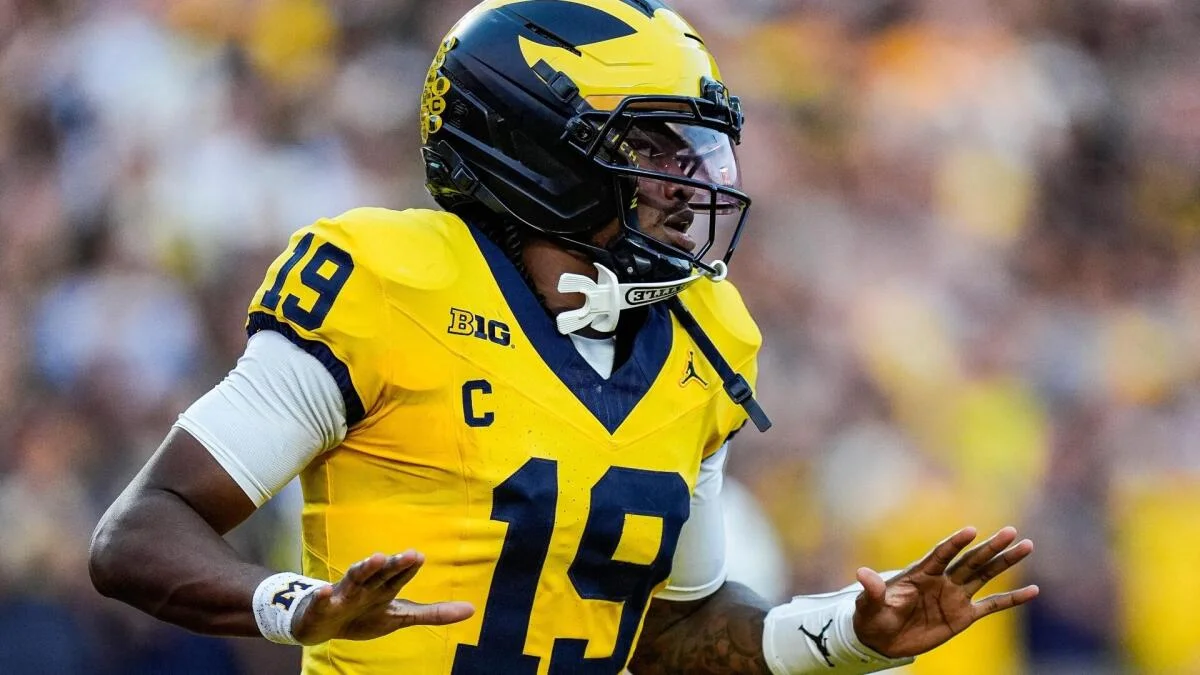 Football player in a yellow jersey and helmet gestures with both hands against a blurred background.