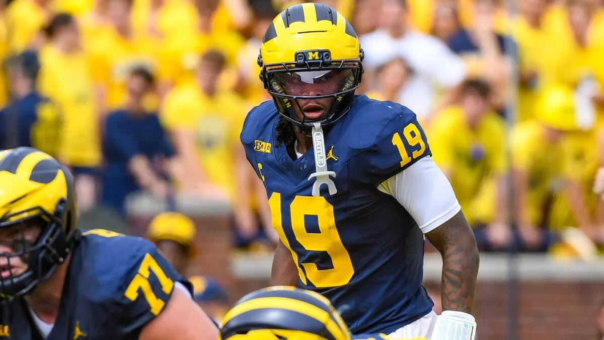 Michigan football player wearing a maize helmet and navy number 19 jersey stands on the field.