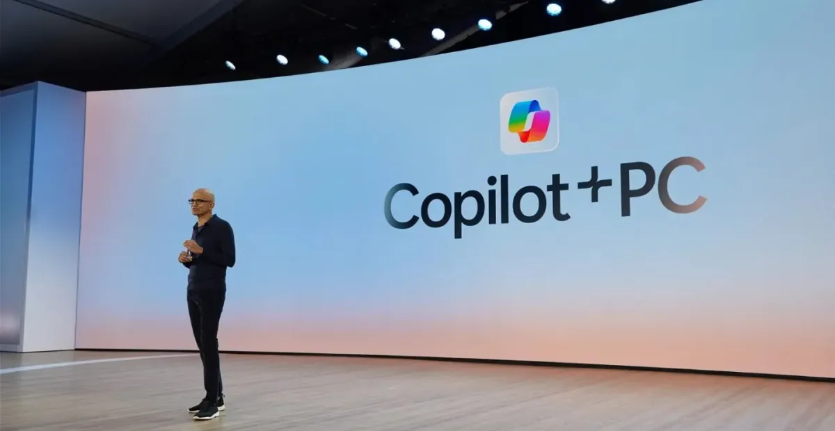 A presenter stands beside a large screen displaying the Copilot+ PC logo in a modern auditorium.