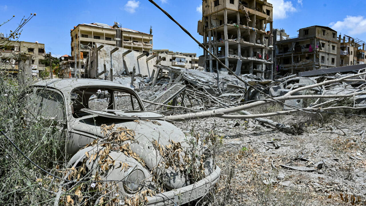 Destroyed buildings and a dust-covered vintage car amid extensive rubble and fallen utility poles