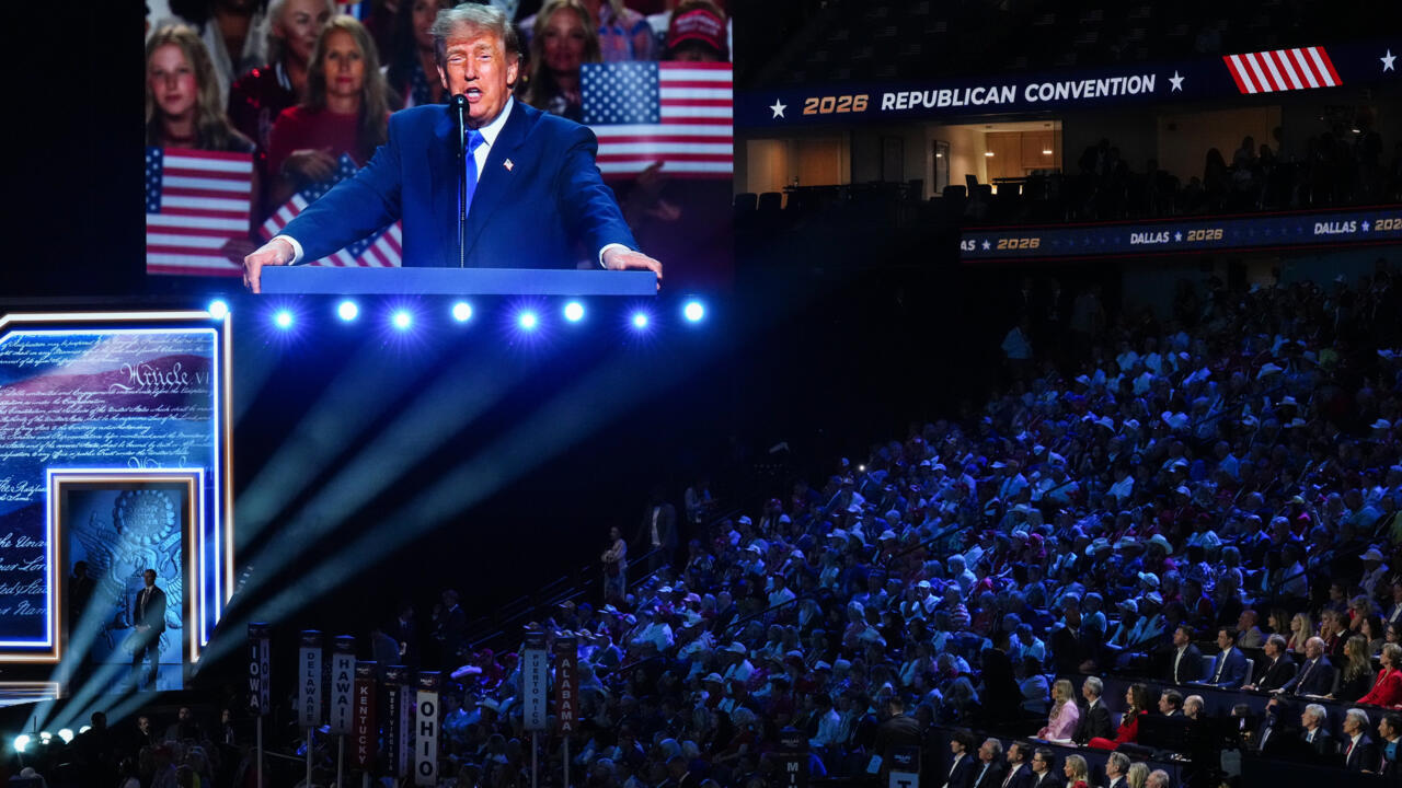 Donald Trump speaks at a podium on a large screen before a crowded Republican convention hall.