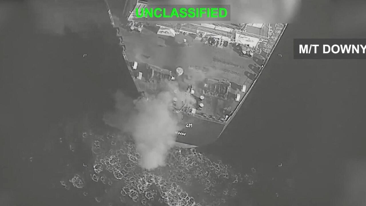 Grayscale aerial view of a vessel near a plume of smoke, with targeting markers and overlays.