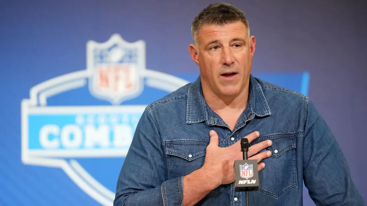 Man in denim shirt speaking into NFL Network microphone with hand over his chest