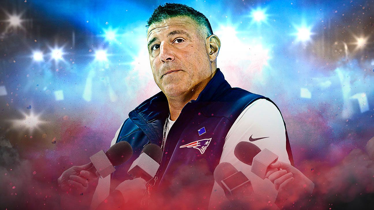 Man in Patriots vest speaking at microphones amid bright blue and red lights