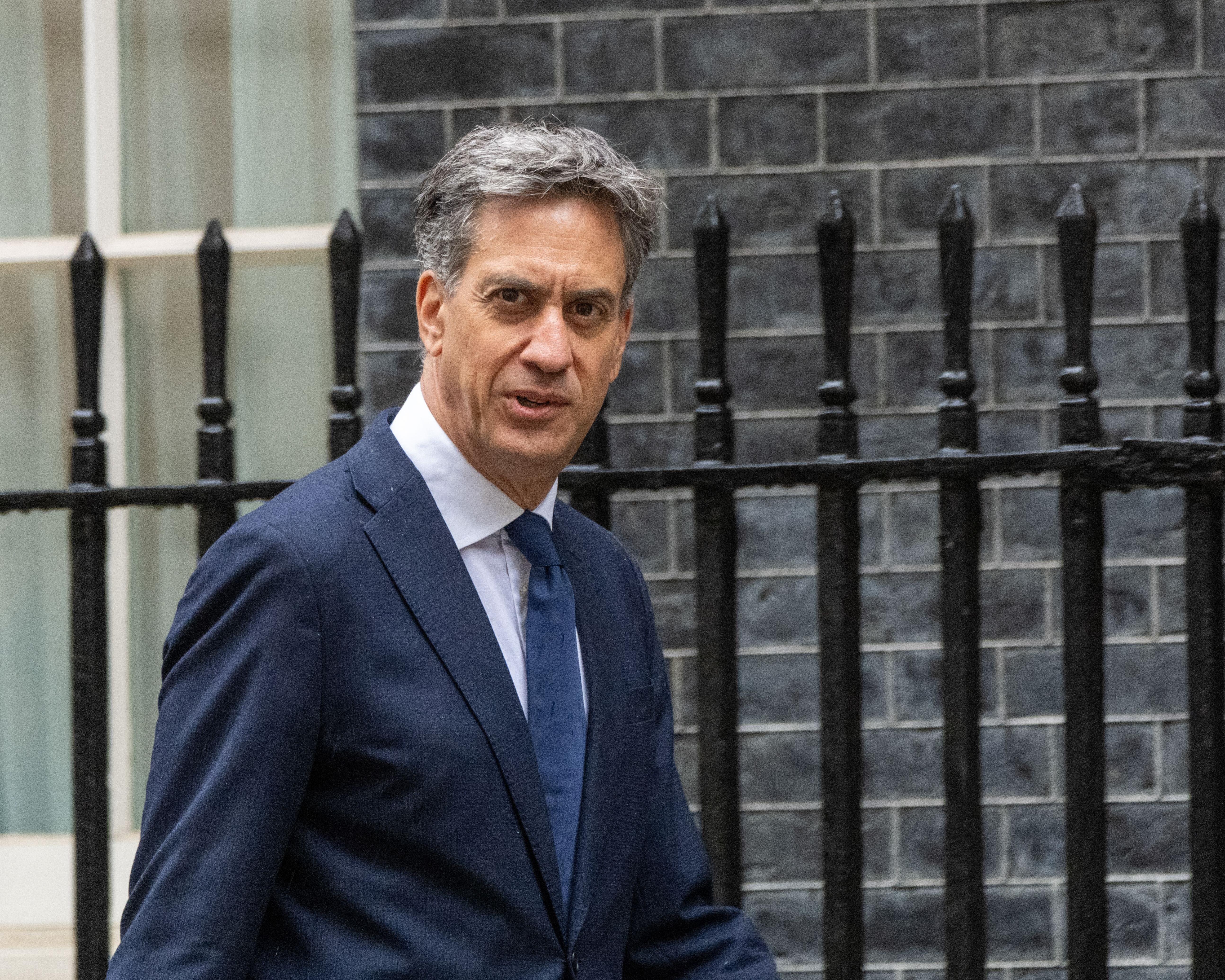Gray-haired man in navy suit and tie standing before a dark brick wall and iron railings