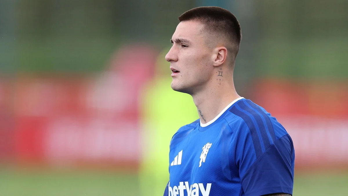 Footballer in blue training jersey standing in profile against a blurred outdoor background