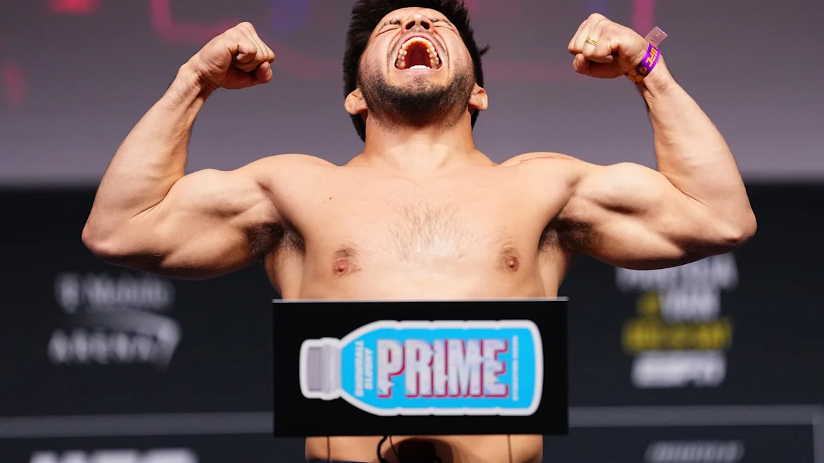 Shirtless fighter raises both arms beside a PRIME-branded scale display at a weigh-in.