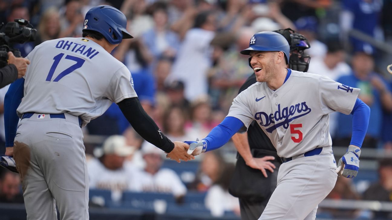 Two Dodgers players in gray uniforms exchange a celebratory handshake during a baseball game.