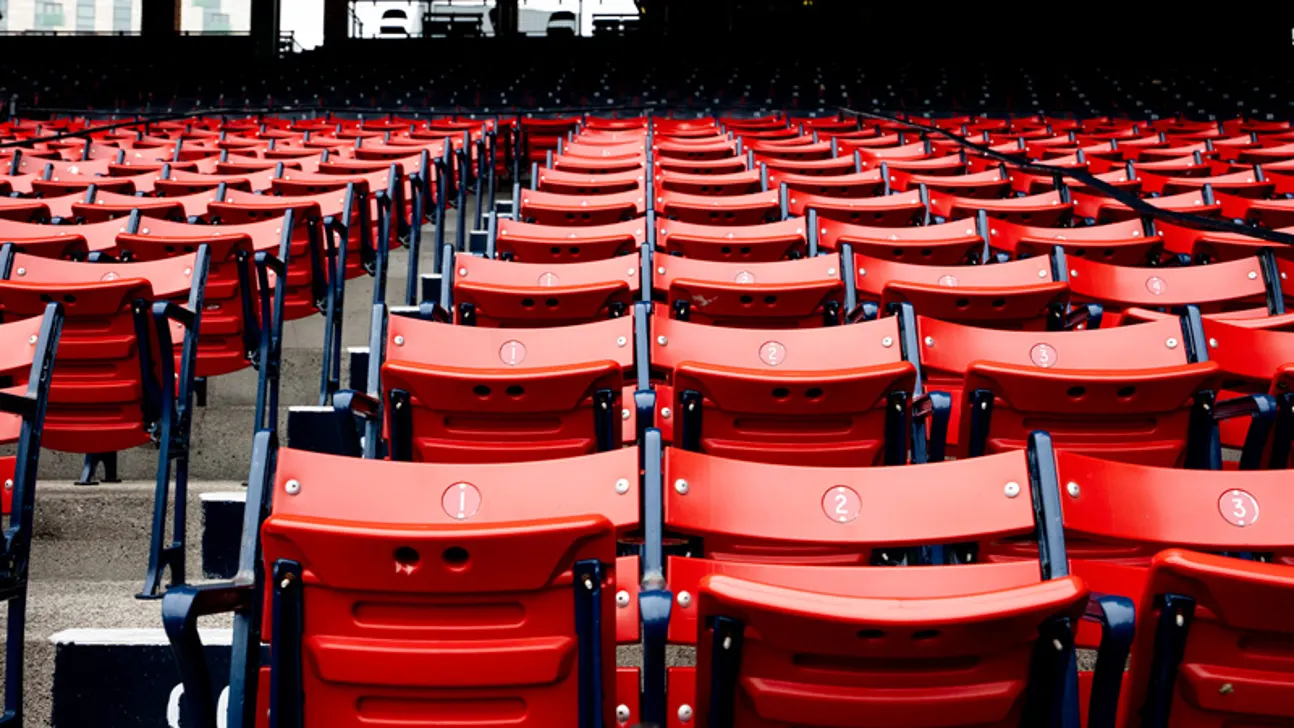 Rows of empty red stadium seats with dark blue frames face a dimly lit field.