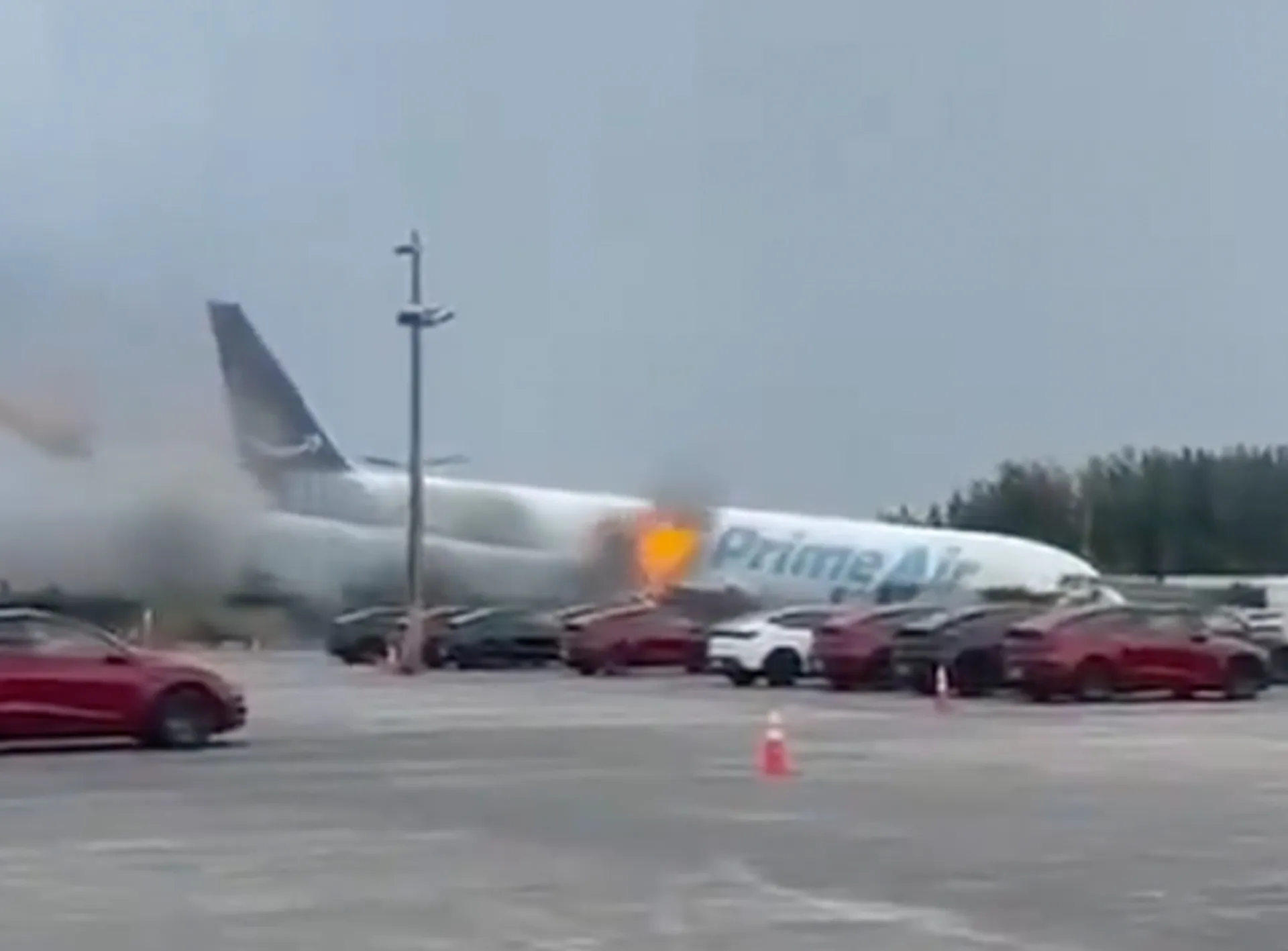 Commercial Amazon-branded cargo plane appears to land amid smoke near parked vehicles.