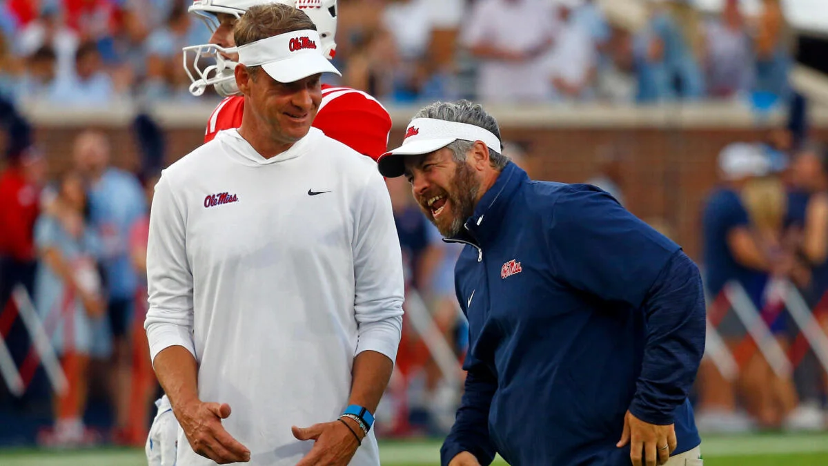 Two Ole Miss football coaches laugh together on the sideline during a game.