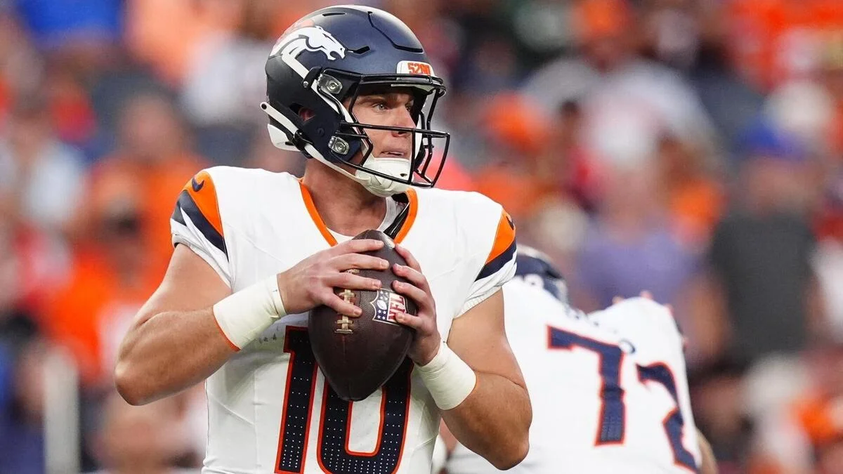 Football quarterback in Broncos uniform holding a ball during a game