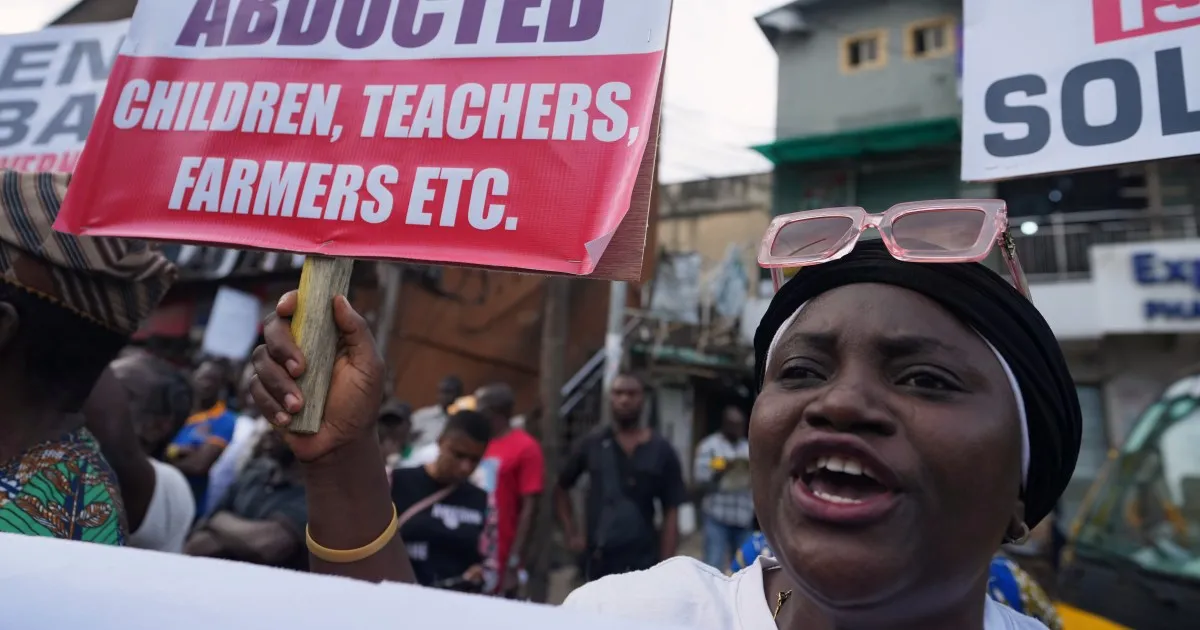 A woman in a black headscarf raises a protest sign reading “Abducted children, teachers, farmers etc.”