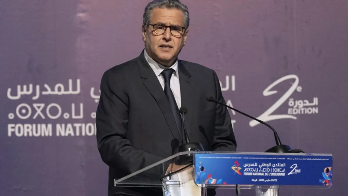 Man in dark suit and glasses speaking at a podium before an Arabic-language forum backdrop