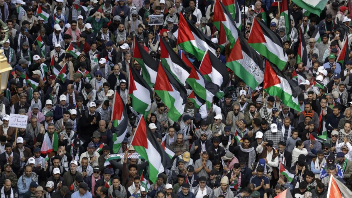 A dense crowd holds Palestinian flags, with many people wearing keffiyeh scarves and caps.