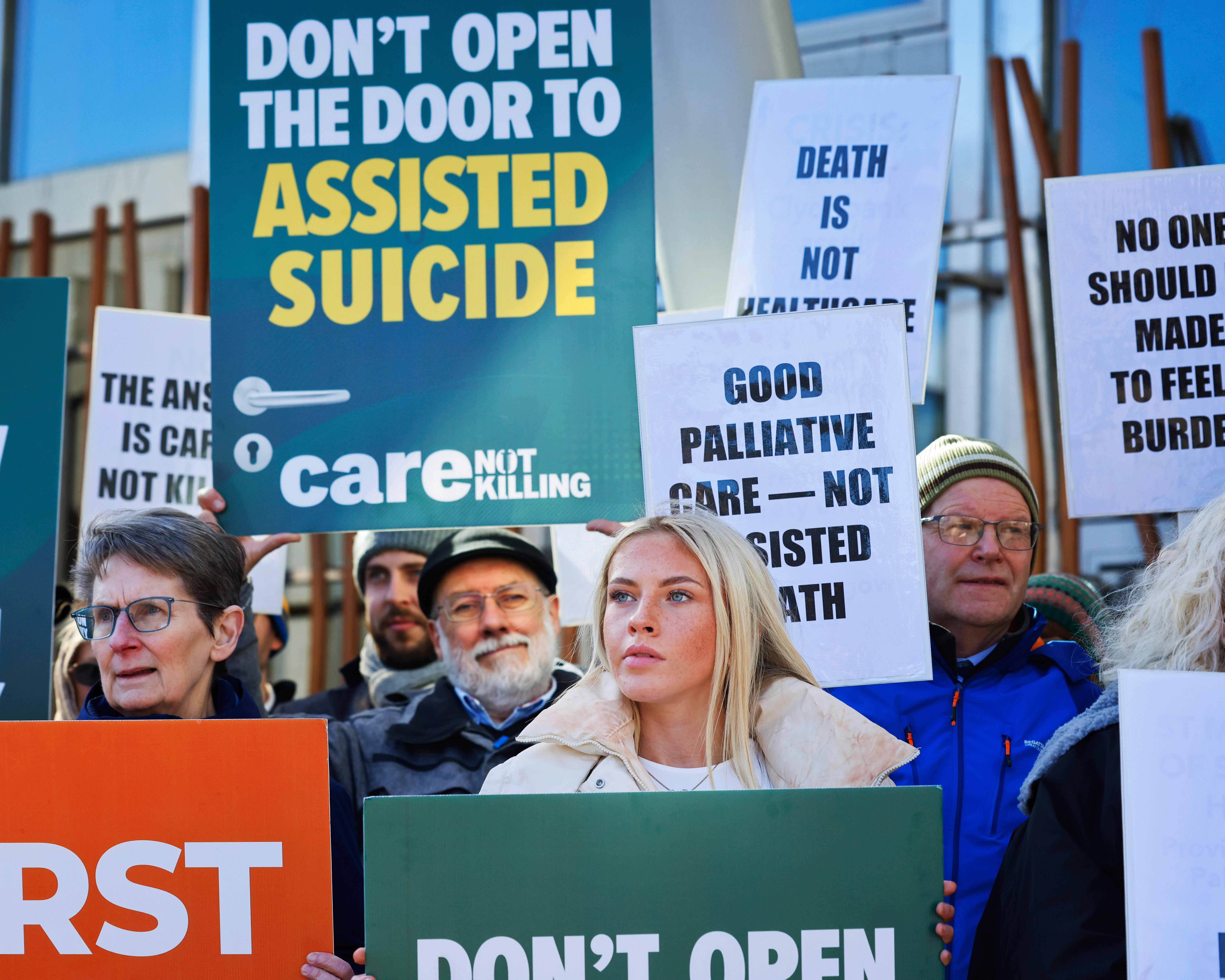 Protesters hold placards opposing assisted dying, including messages supporting palliative care.