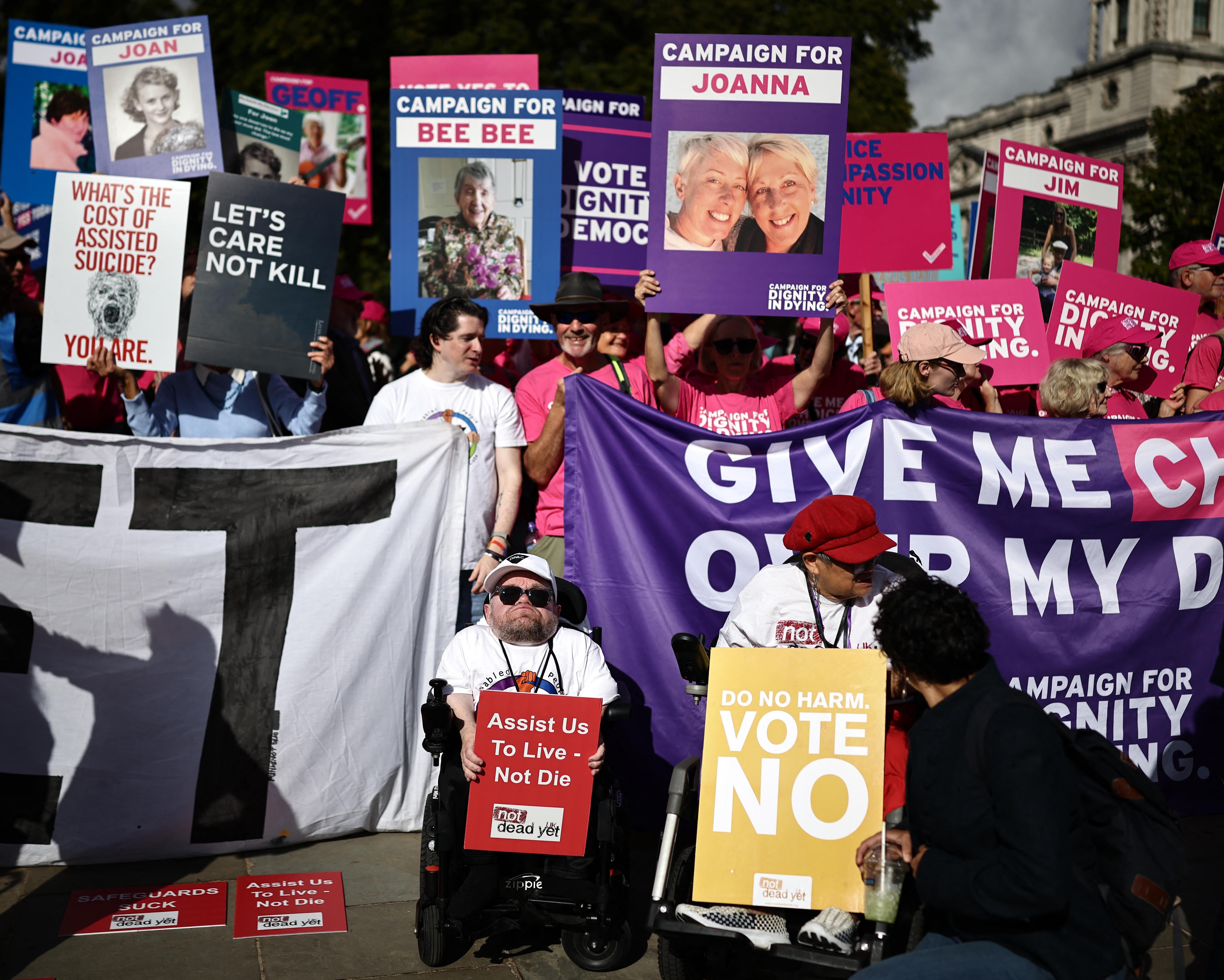 Crowd holds colorful campaign placards and banners during a protest about assisted dying.