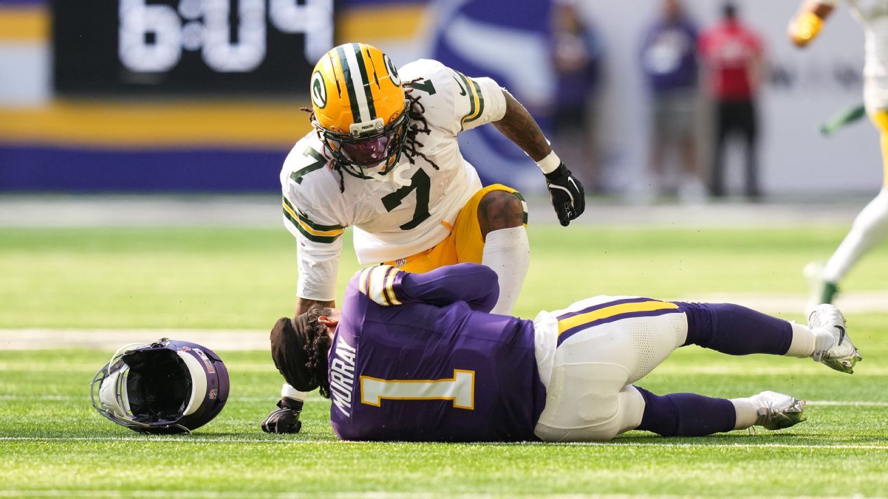 Football player in purple lies on the field as a Packers defender kneels nearby