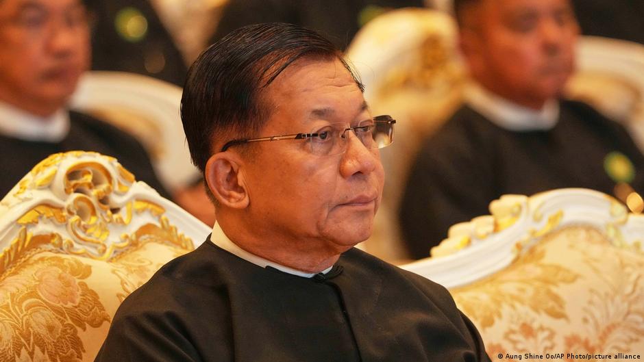 Man in black formal attire and glasses seated in an ornate chair at a formal gathering