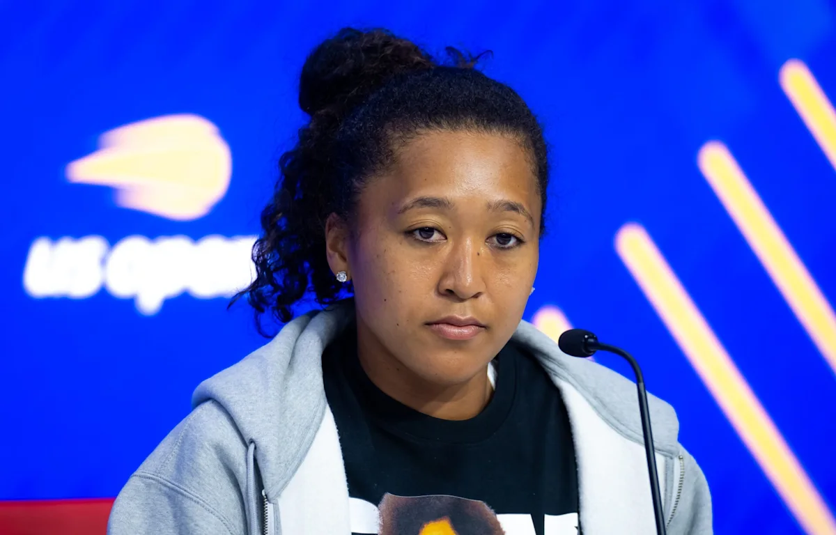 Tennis player speaking into a microphone at a press conference against a blue backdrop