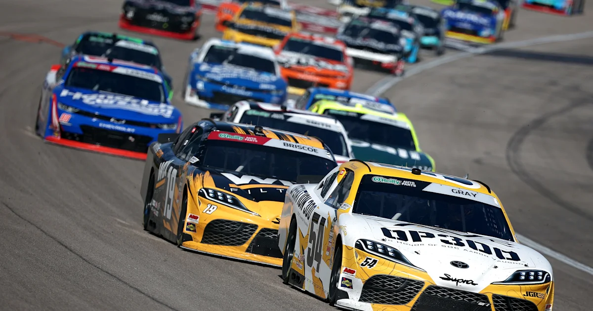 Stock cars race in a close pack, with white and yellow cars leading on an oval track.