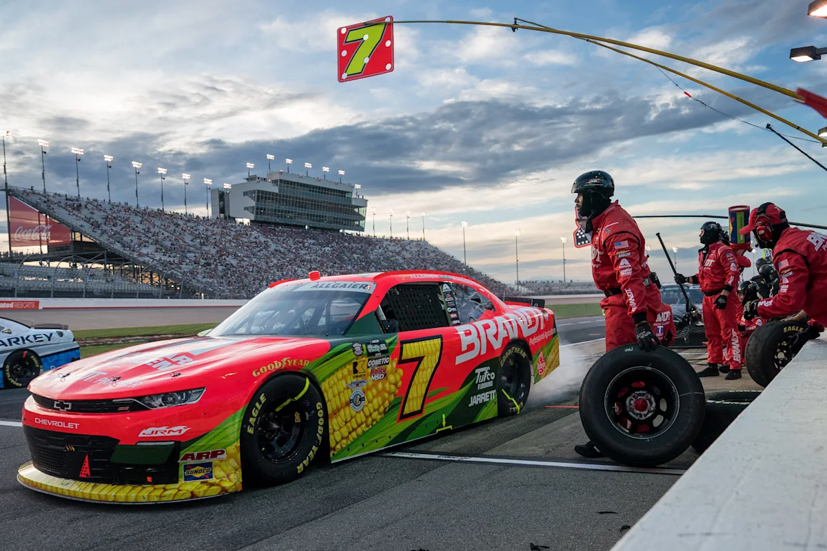 A red No. 7 stock car stops for a pit stop as crew members prepare tires.