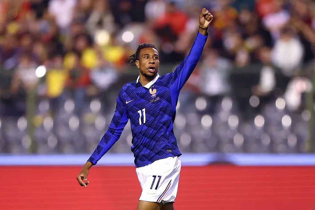 France player in a blue number 11 jersey raises his fist before a blurred stadium crowd.