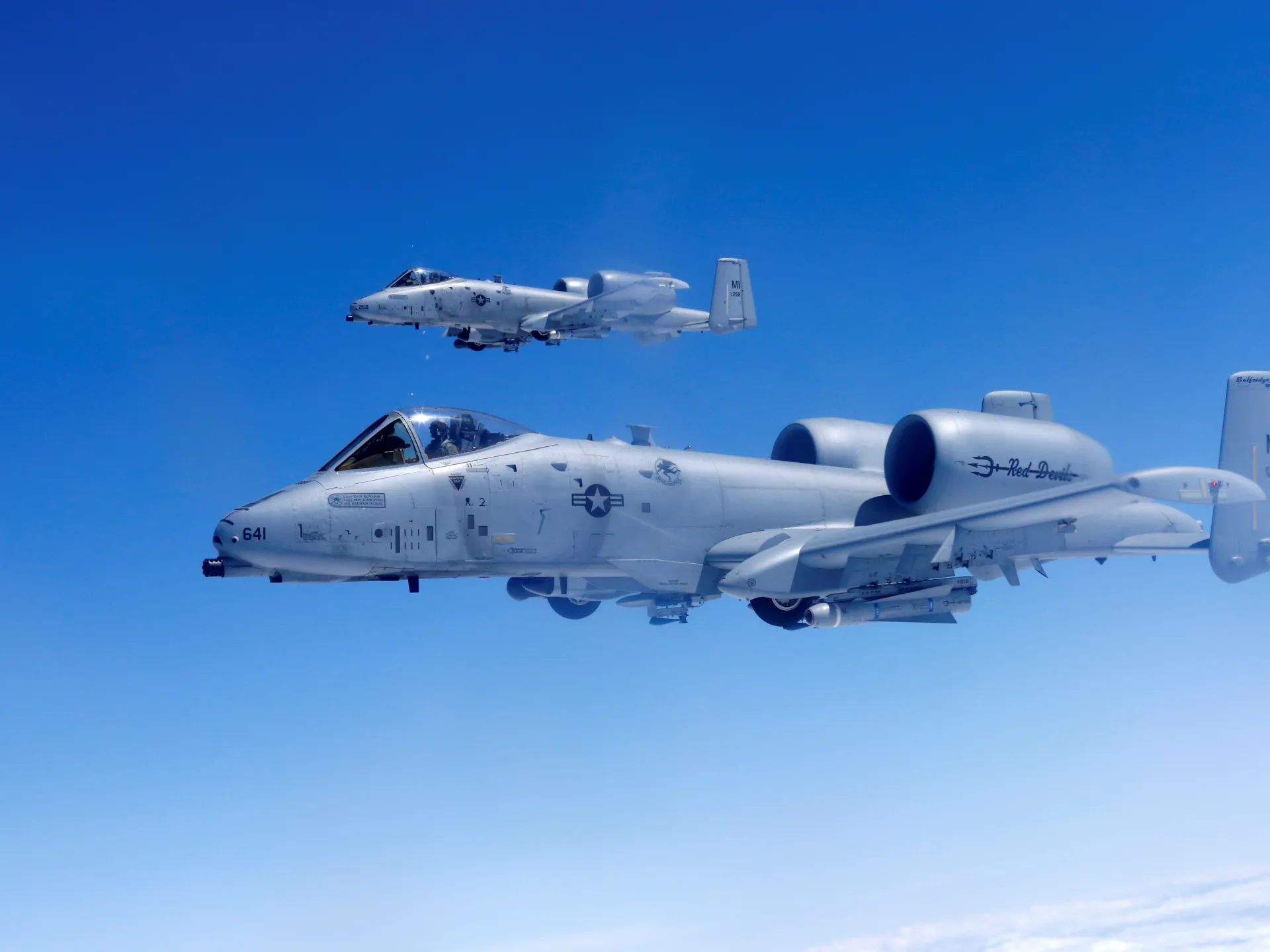 Two military jets fly in formation against a clear blue sky