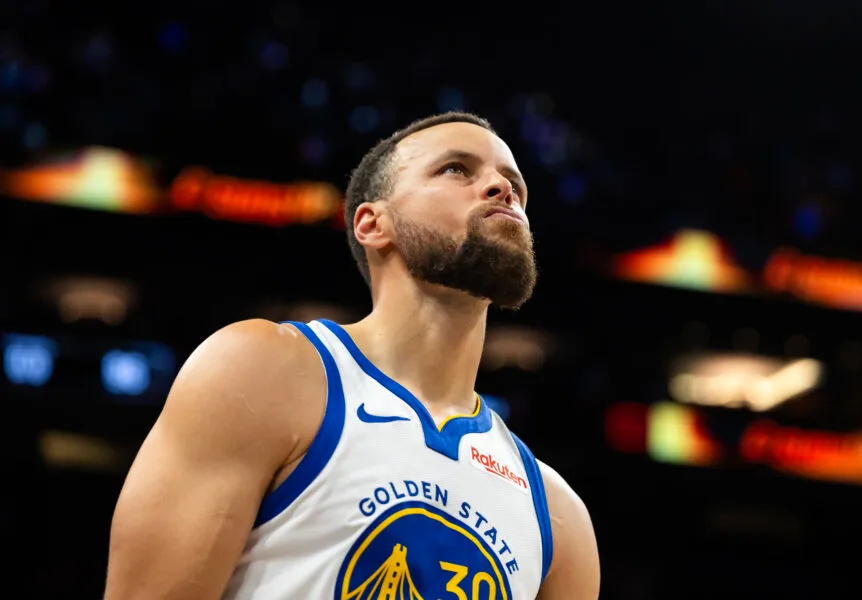 Basketball player in a white and blue Golden State jersey looks upward during a game.