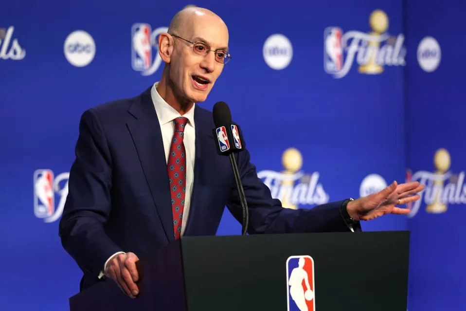 Bald man in suit speaks at an NBA podium before a Finals backdrop.